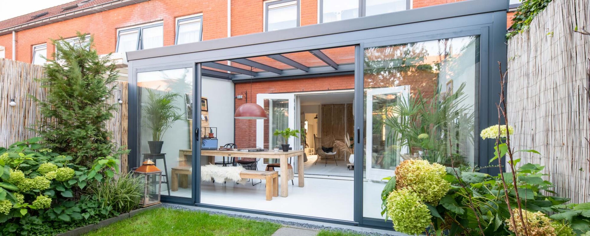 Moderne schuifpui in aluminium overkapping, biedt een lichte verbinding tussen tuin en leefruimte in een rijtjeshuis.